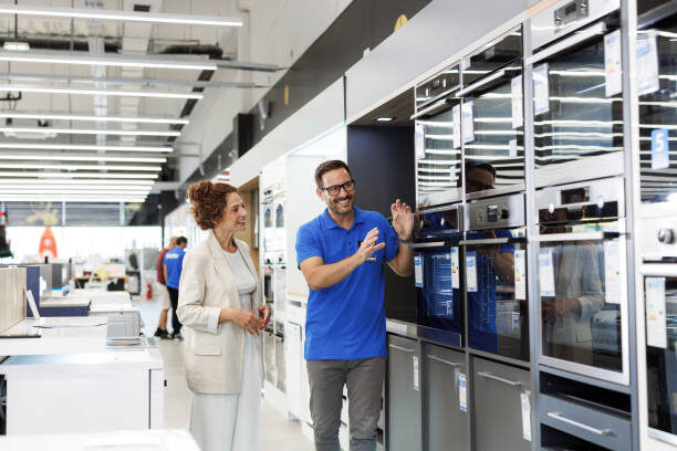 Friendly salesperson showcases the features of modern appliances to a customer in a bright, spacious store. Emphasis on customer service and technology.