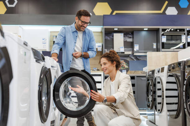 A couple happily examines a washing machine in a modern appliance store. They appear satisfied with their choice, representing a positive shopping experience.